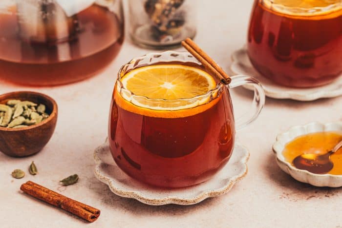 A glass of chai vanilla bean hot toddy with cinnamon sticks surrounding it. 
