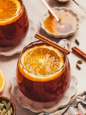 A glass mug filled with chai vanilla bean hot toddy and garnished with orange slices.