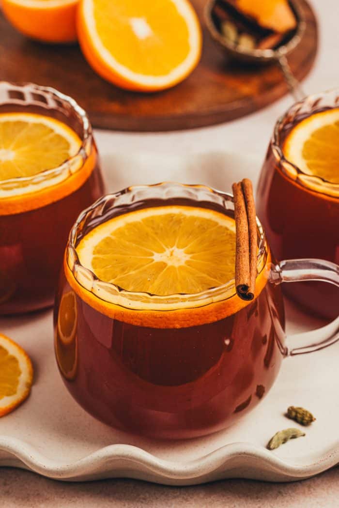 A couple of glass mugs filled with chai vanilla bean hot toddy and garnished with orange slices.