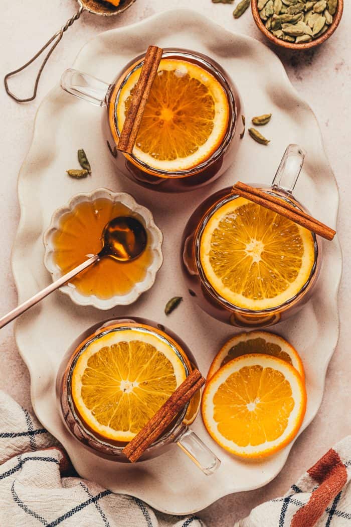 A couple of glass mugs filled with chai vanilla bean hot toddy and garnished with orange slices.
