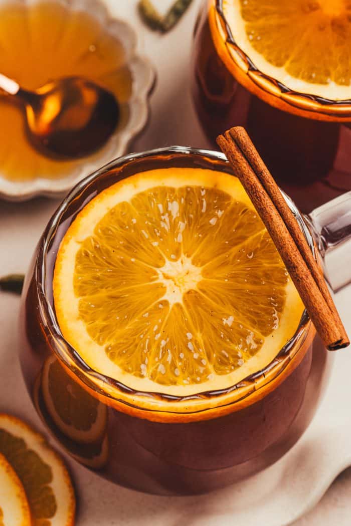 A glass mug filled with chai vanilla bean hot toddy and garnished with orange slices.