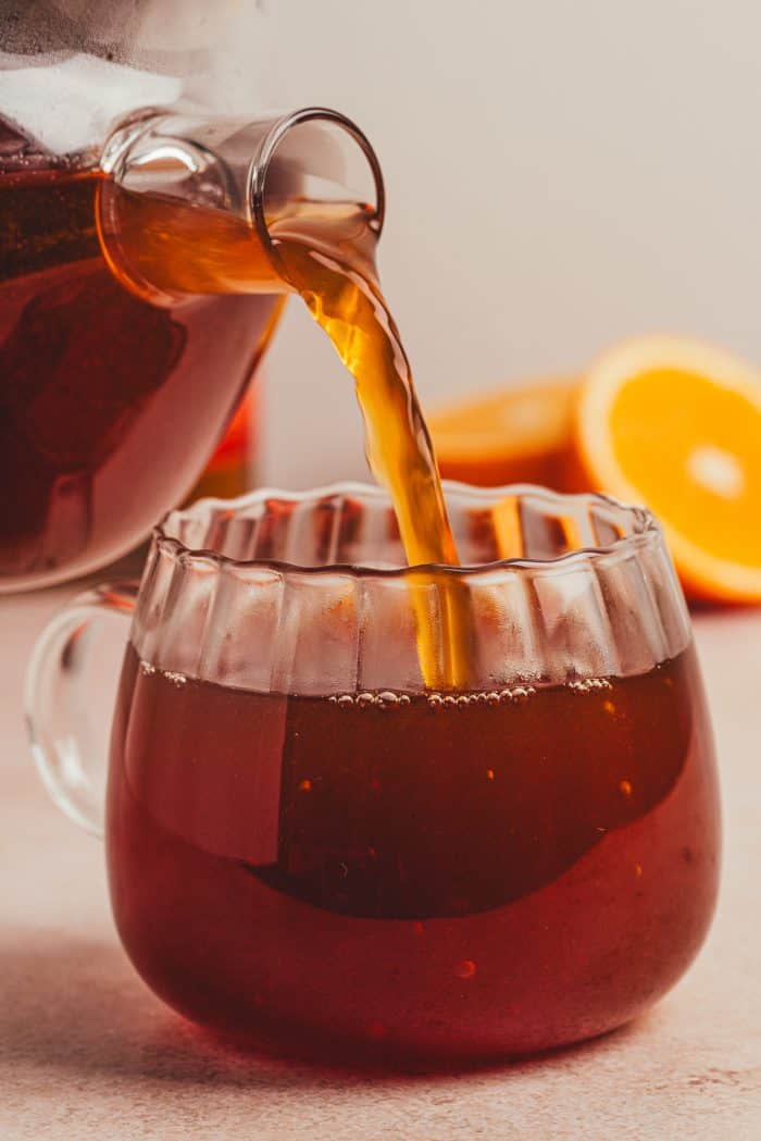 The chai hot toddy mixture being poured into a glass mug. 