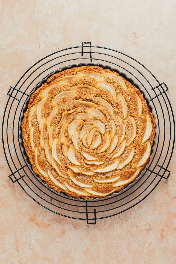 A baked hazelnut Frangipane Pear Tart on a cooling rack.