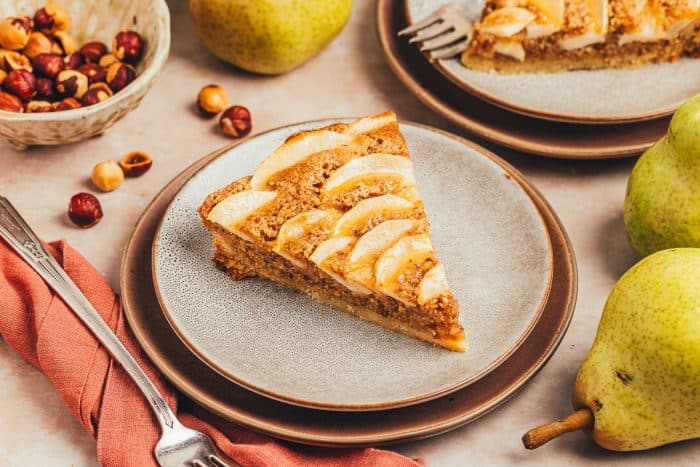 A slice of pear tart on two white plates with pears in the background.
