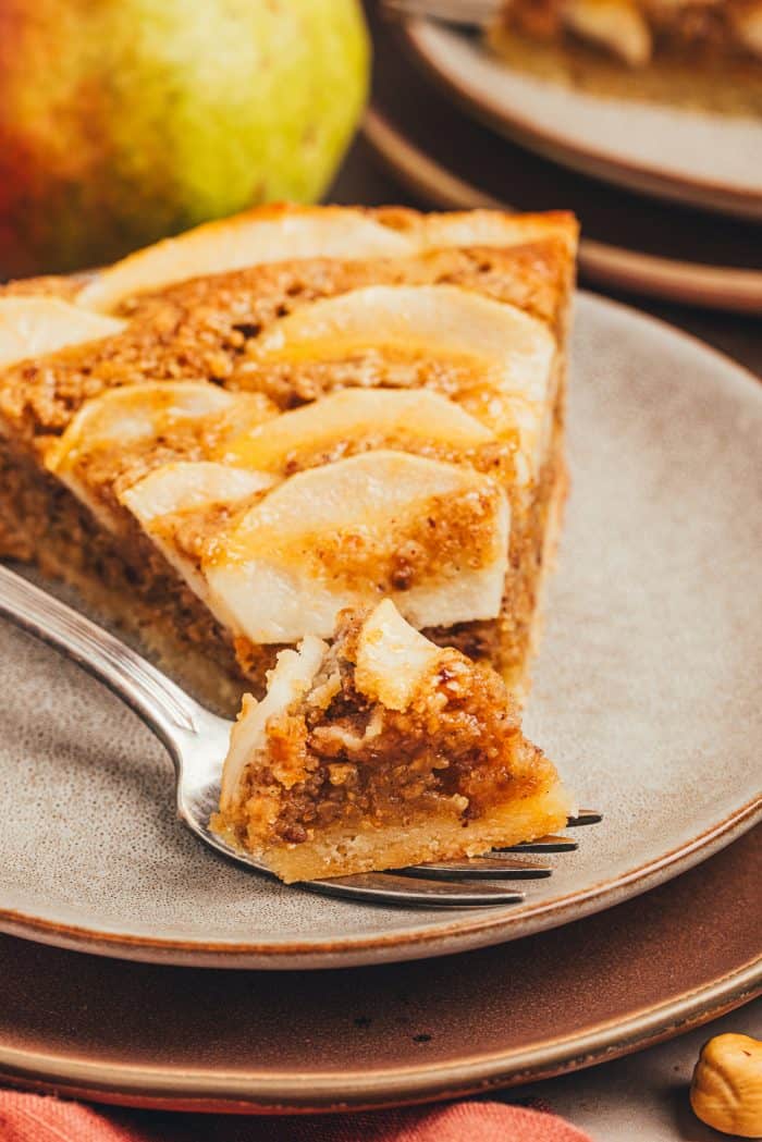 A slice of pear frangipane tart on a plate with a bite taken out of it.