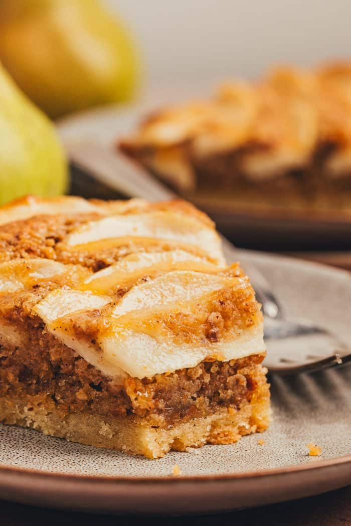 A slice of pear frangipane tart on a plate with a bite taken out of it. 