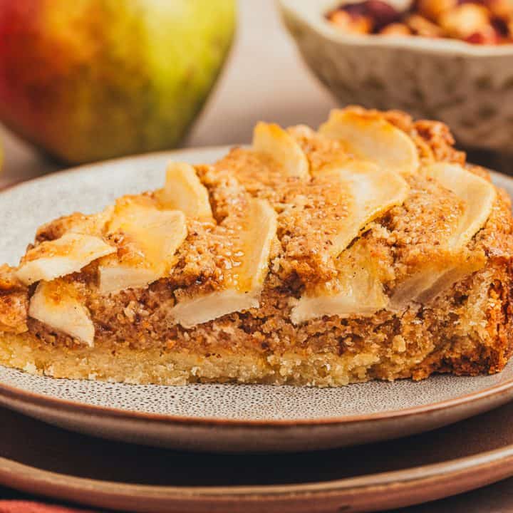 A slice of pear tart on two white plates with pears in the background.