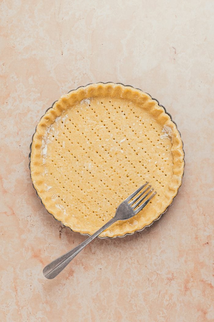 The unbaked tart shell crust being pricked by a fork.