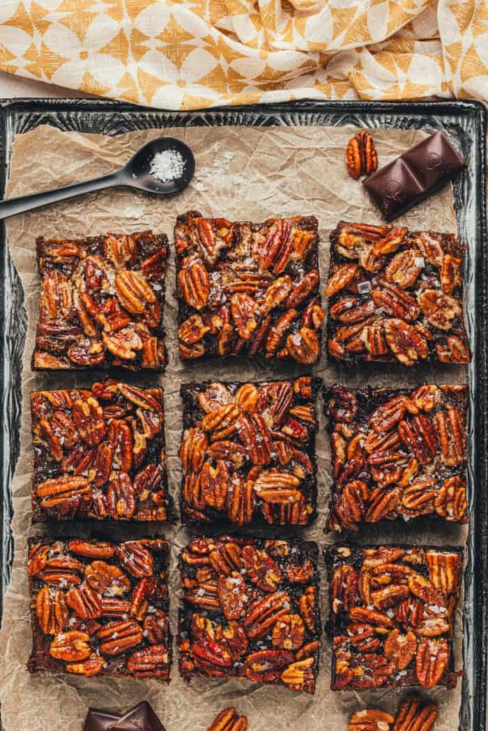 Brownies with a pecan pie topping are sliced and displayed on parchment paper.
