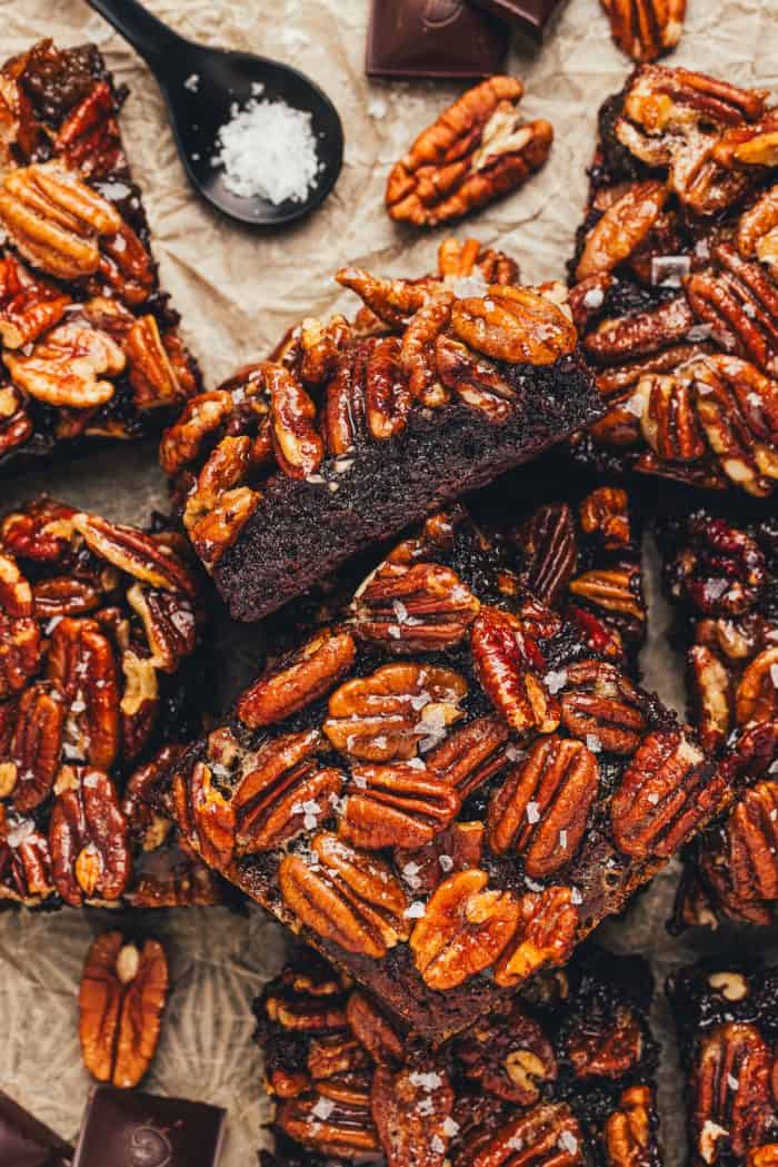 Various pecan pie brownies are scattered in a pile on parchment paper. 