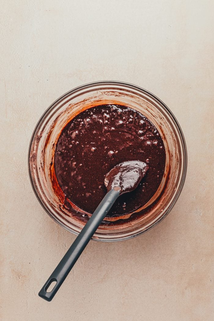 The sugar and flour mixture added to the melted chocolate mixture in a glass bowl.