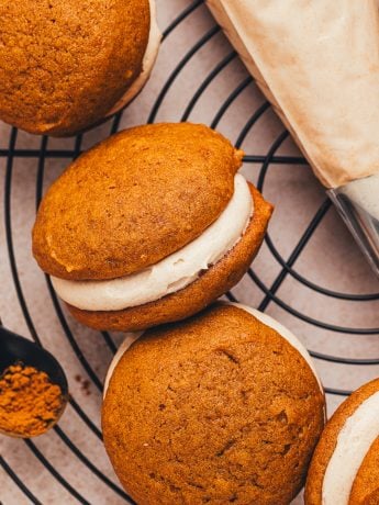 Pumpkin whoopie pies filled with cinnamon cream cheese filling on a cooling rack.