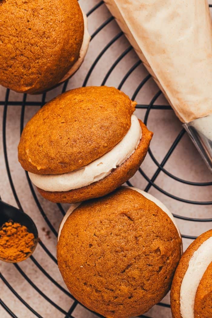 Pumpkin whoopie pies filled with cinnamon cream cheese filling on a cooling rack.