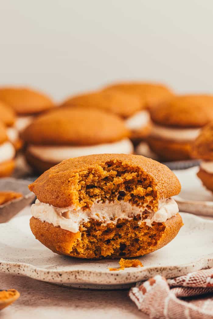 A pumpkin spice whoopie pies with a bite taken out of it on a plate.
