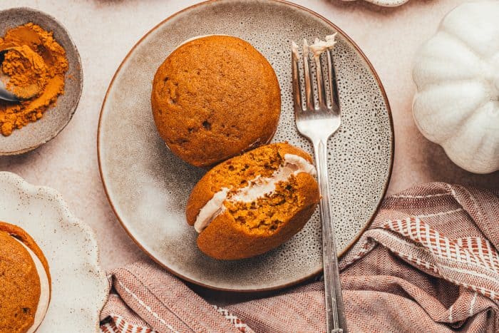 Two whoopie pies on a plate and one has a bite taken out it and a fork is on the plate.
