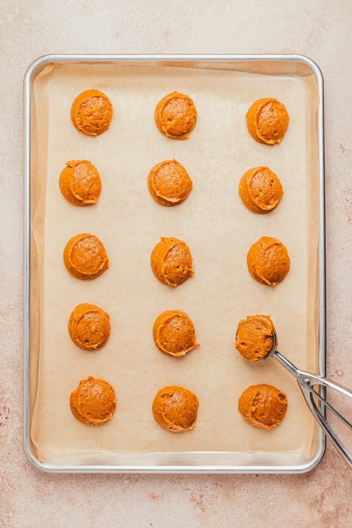Unbaked pumpkin whoopie pie pieces on a baking sheet with parchment paper.