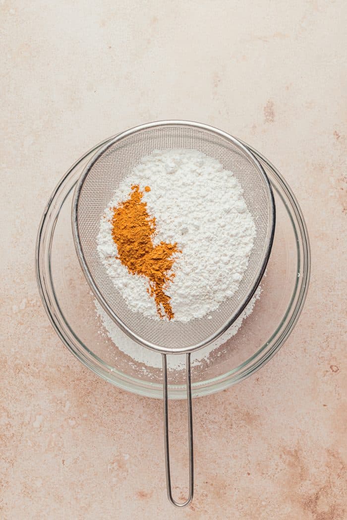 Flour and cinnamon being sifted into a glass bowl.
