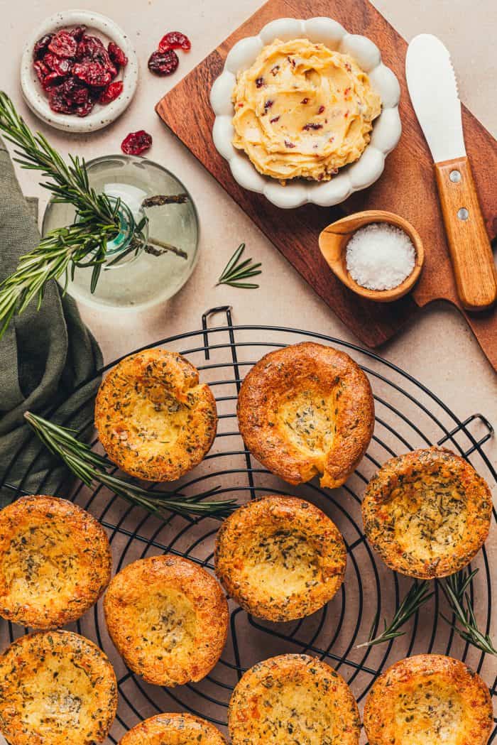 A few brown butter popovers on a cooling rack with a bowl of butter in the background.