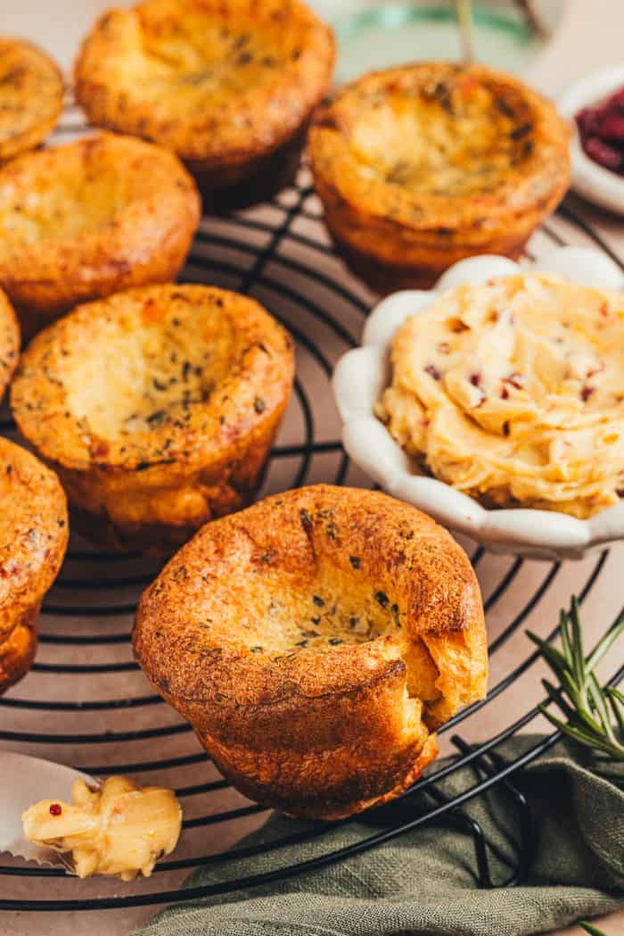 A few brown butter popovers on a cooling rack with a bowl of butter in the background.