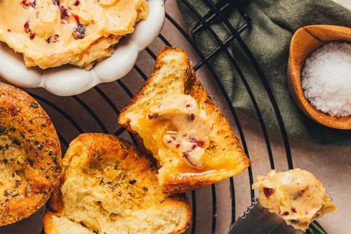 A few brown butter popovers on a cooling rack with a bowl of butter in the background.