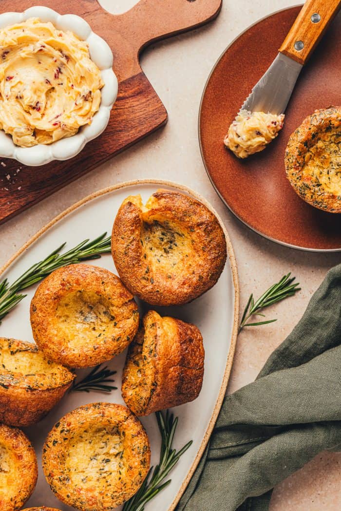 A few herb popovers on a platter with a bowl of butter in the background.