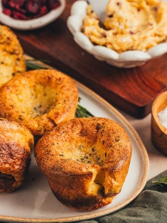 A few brown butter popovers on a platter with a bowl of butter in the background.