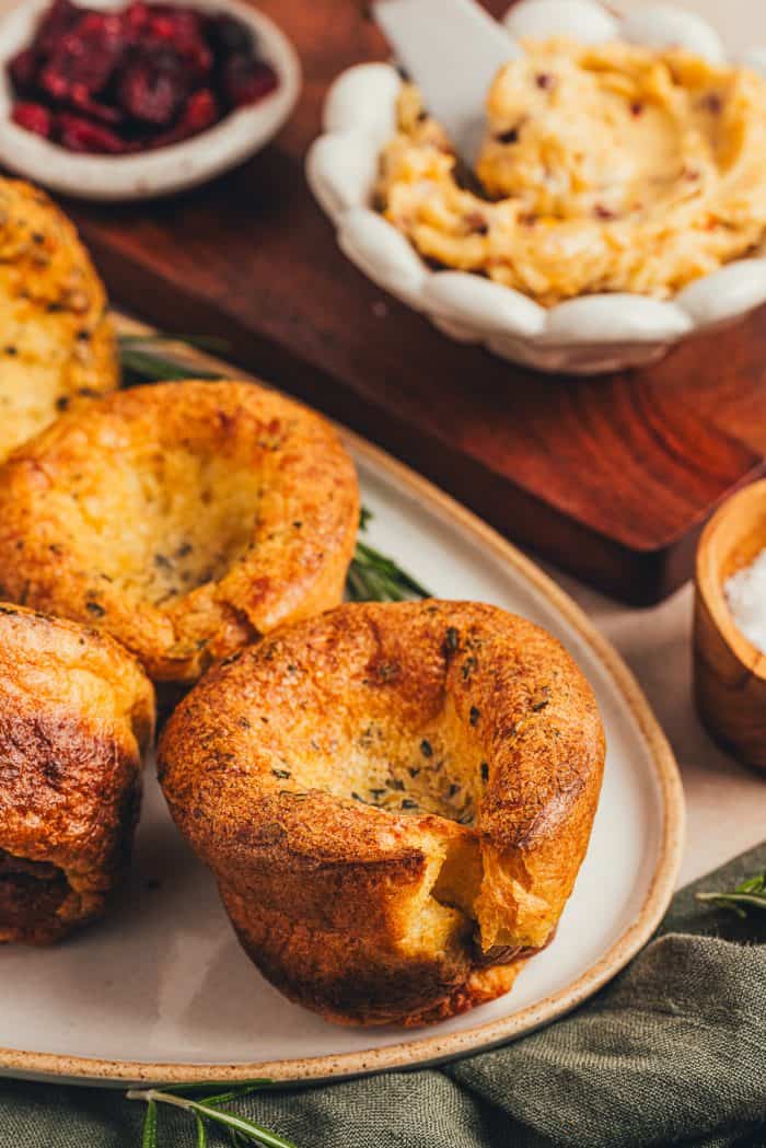 A few brown butter popovers on a platter with a bowl of butter in the background.