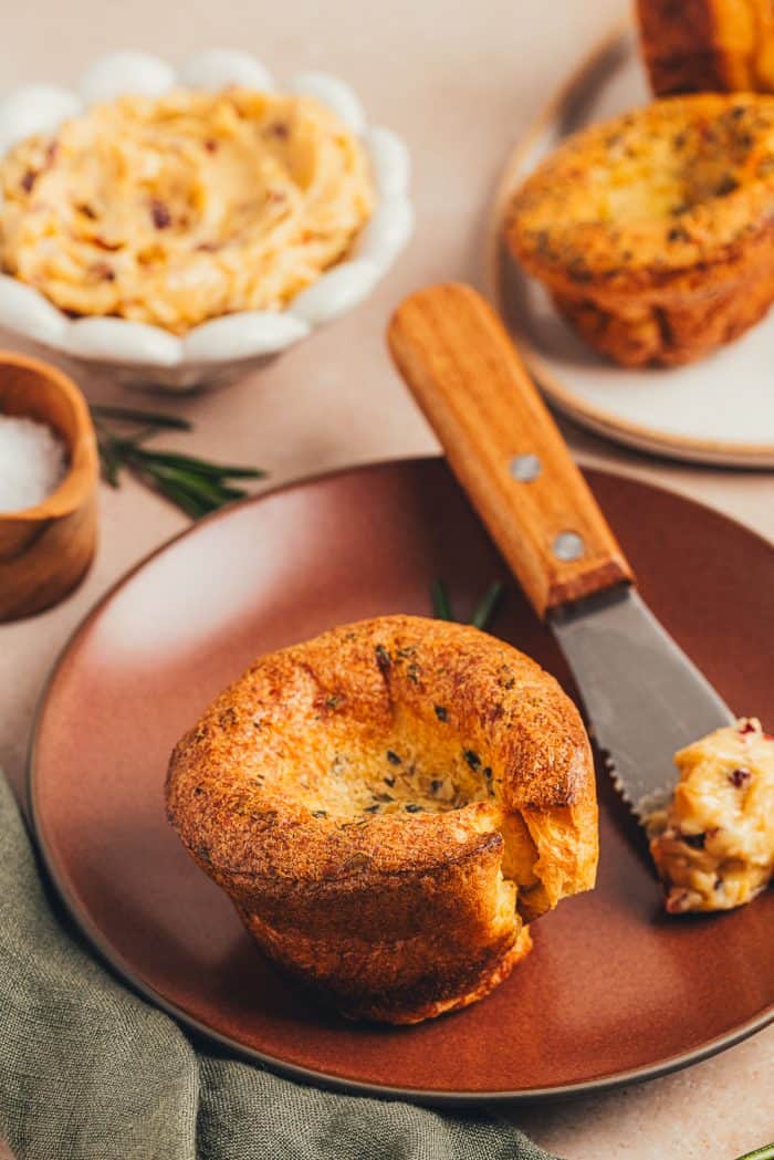 A rosemary popover on a plate with a knife with butter.