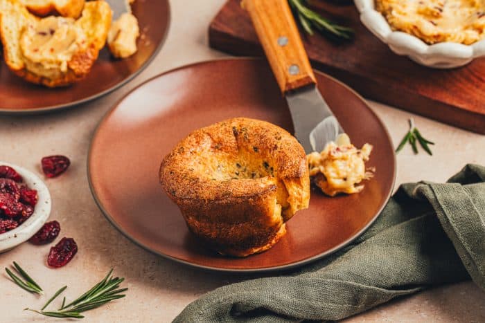 A rosemary popover on a plate with a knife with butter.