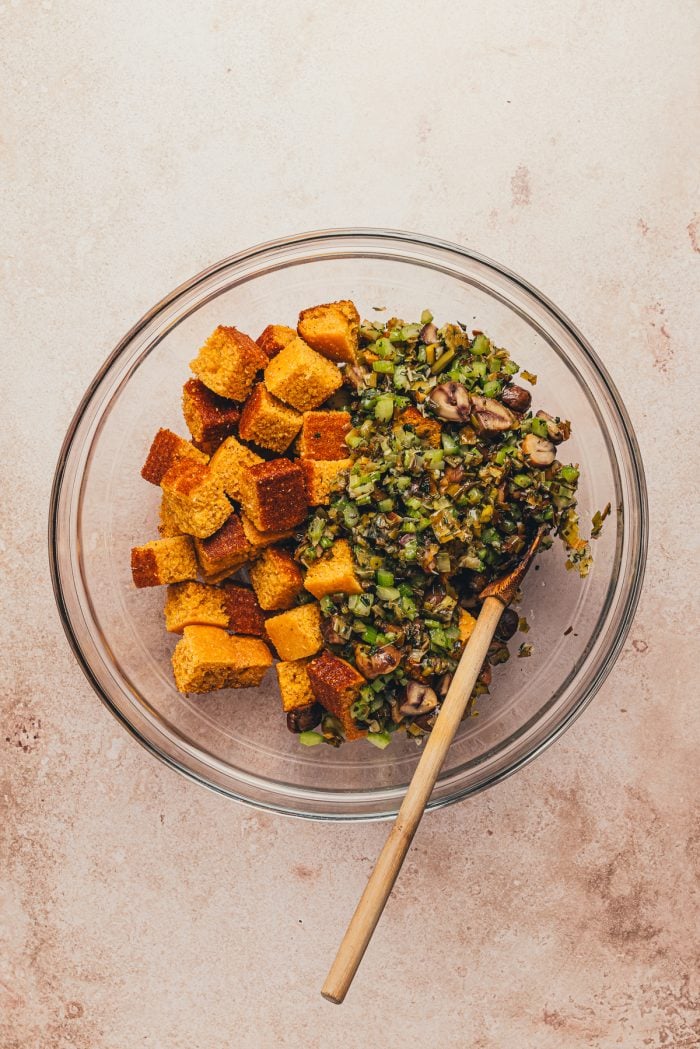 A glass bowl with dried out cornbread cubes and the cooked vegetable mixture.