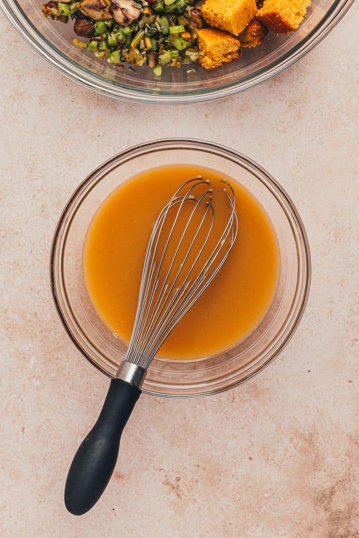 A glass bowl with broth mixed with eggs and a whisk.