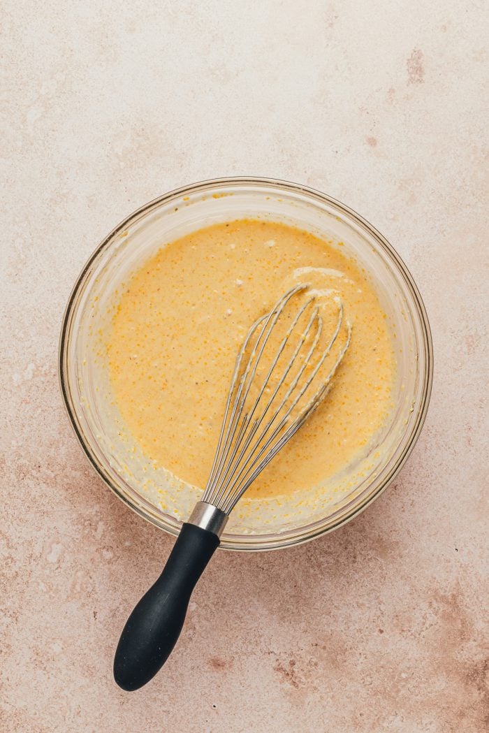 A glass bowl with the cornbread batter and a whisk.