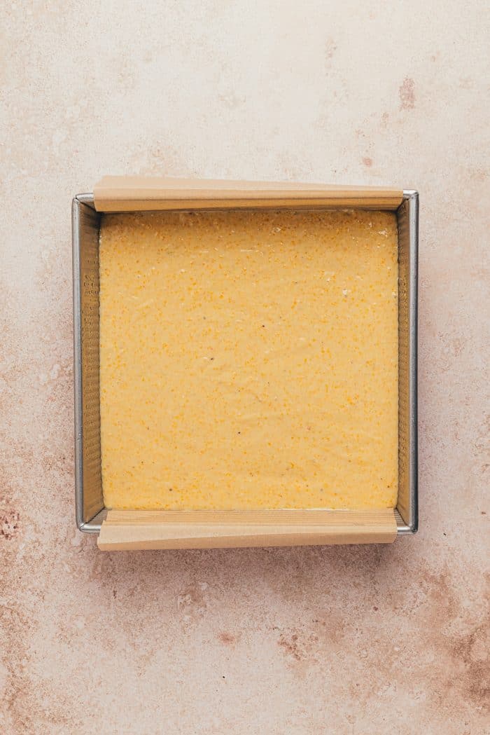 A baking pan with parchment paper and cornbread batter.