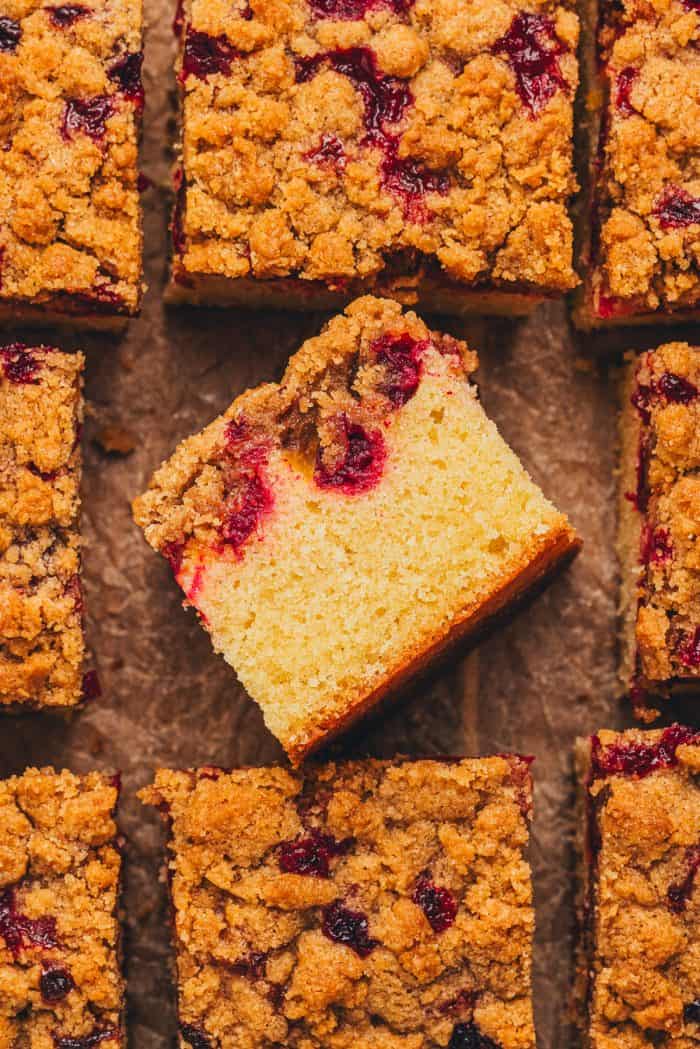 The top view of a cranberry crumb cake sliced and one slice is turned on it's side to show the layers of the cake.