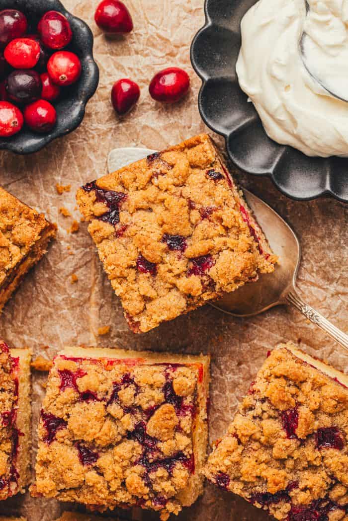 The top view of a cranberry crumb cake sliced with a bowl of creme fraiche and a smaller bowl of cranberries.