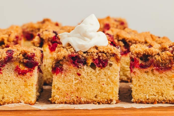 Slices of cranberry crumb cake and one has whipped cream on top.