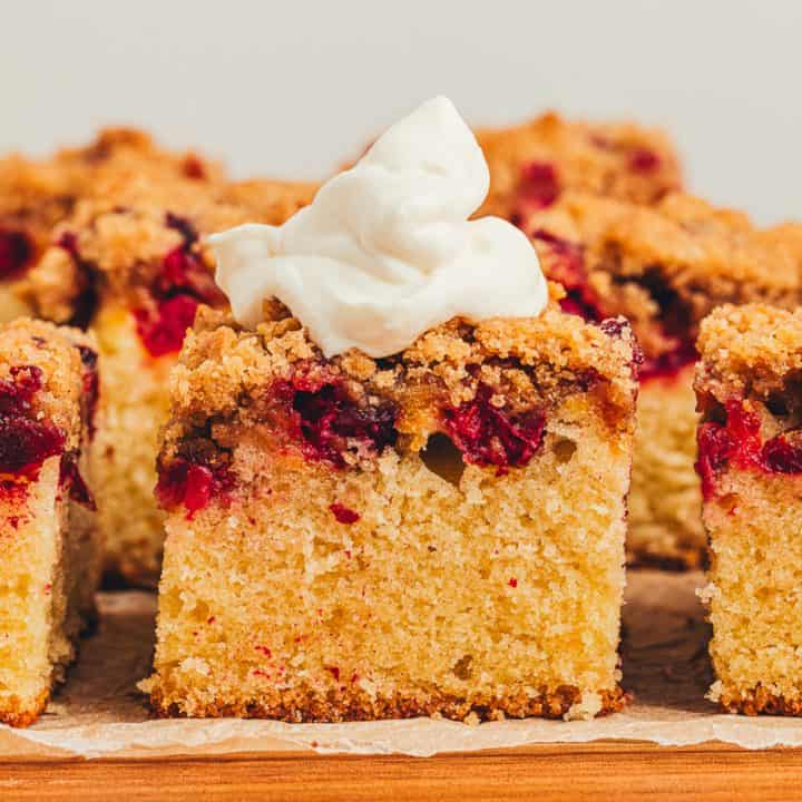 Slices of cranberry crumb cake and one has whipped cream on top.