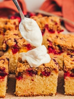 A variety of sliced cranberry crumb cake with one slice receiving a dollop of cream fraiche.