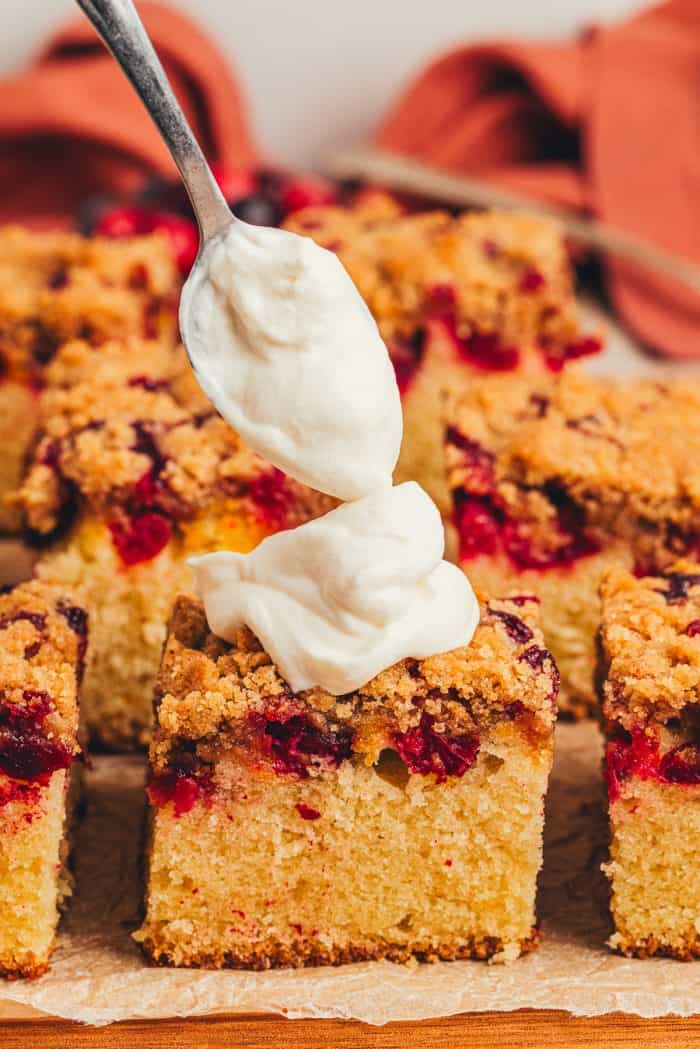 A variety of sliced cranberry crumb cake with one slice receiving a dollop of creme fraiche.