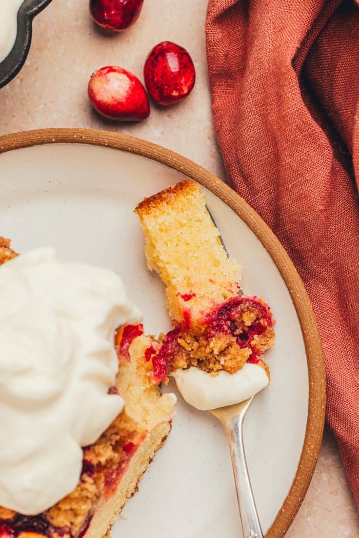 A slice of cranberry crumb cake on a small dessert plate with a fork and a piece of the cake bitten into.