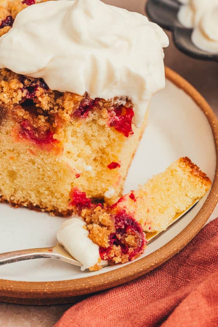 A slice of cranberry crumb cake on a small dessert plate with a fork and a piece of the cake bitten into.