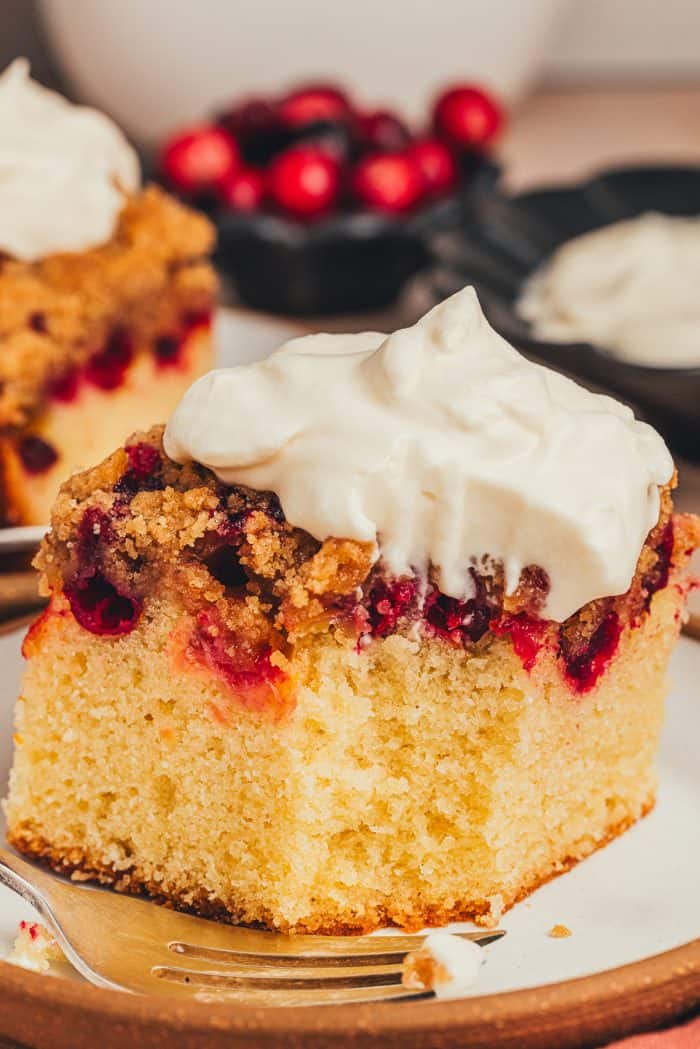 A slice of cranberry crumb cake on a small dessert plate with a fork and a piece of the cake bitten into.