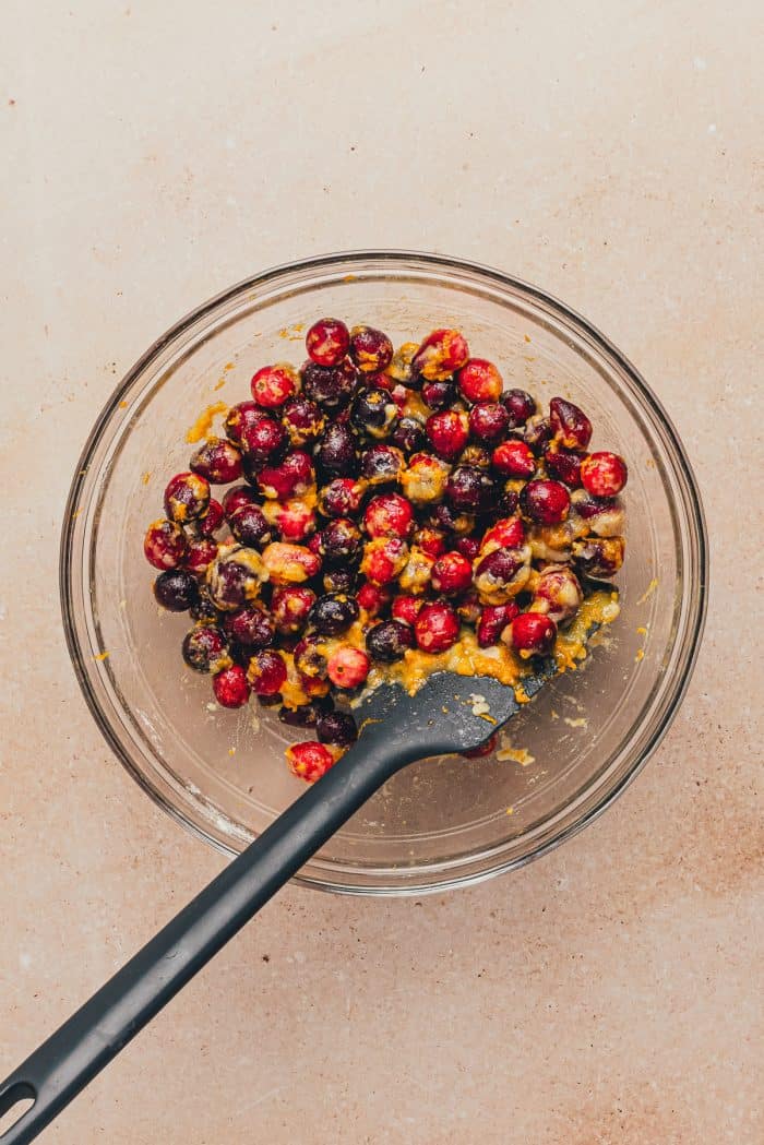A glass bowl with the cranberries and orange zest and a spatula.