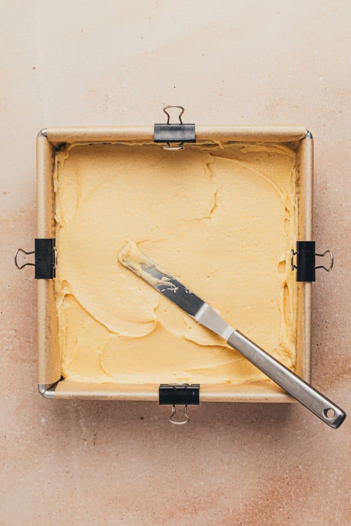 A square baking pan with parchment paper and a layer of cake batter.