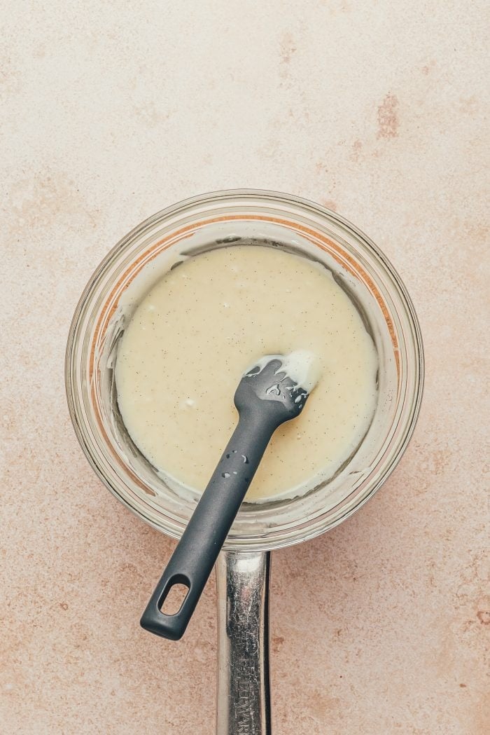 The melted white chocolate filling in a glass mixing bowl with a spatula.