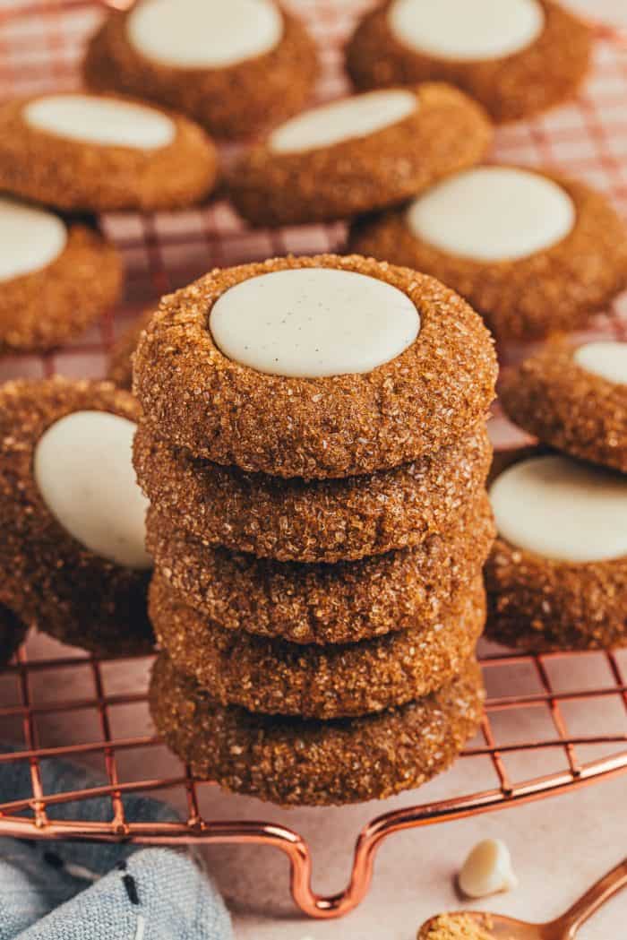 A variety of gingerbread thumbprint cookies on a cooling rack with a stack of thumbprint cookies.