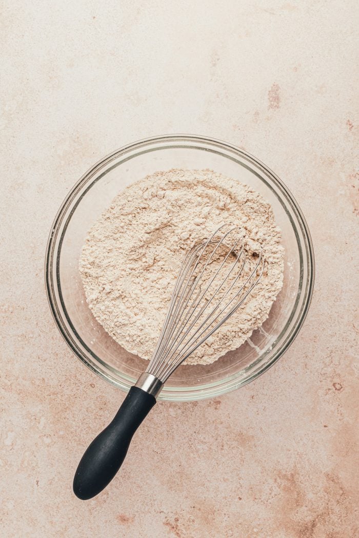 A glass bowl with the dry ingredients mixed together and a whisk.