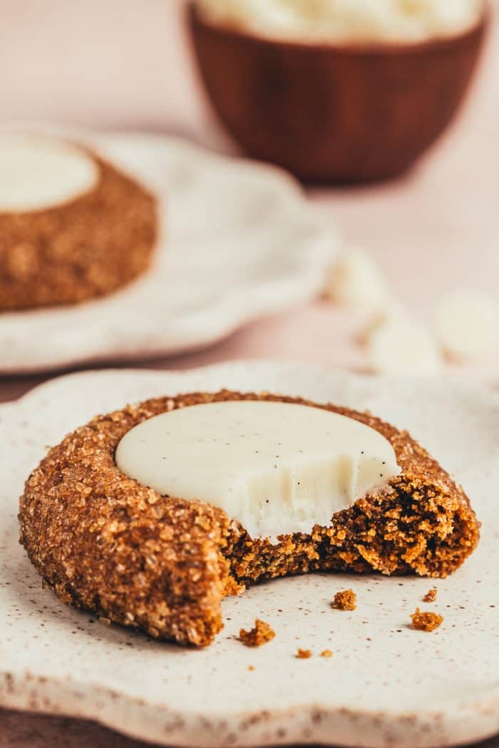 A plate with a thumbprint cookie on it with a bite taken out of it. 