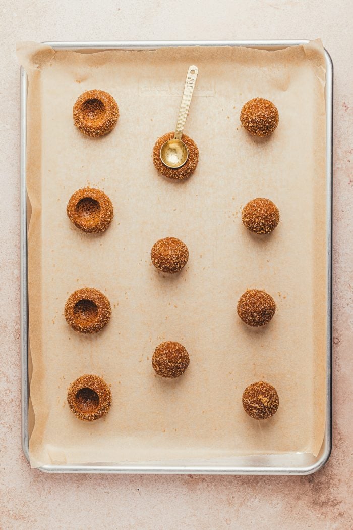 The thumbprint cookie dough placed on cookie sheets with a spoon being used to create the thumbprint.