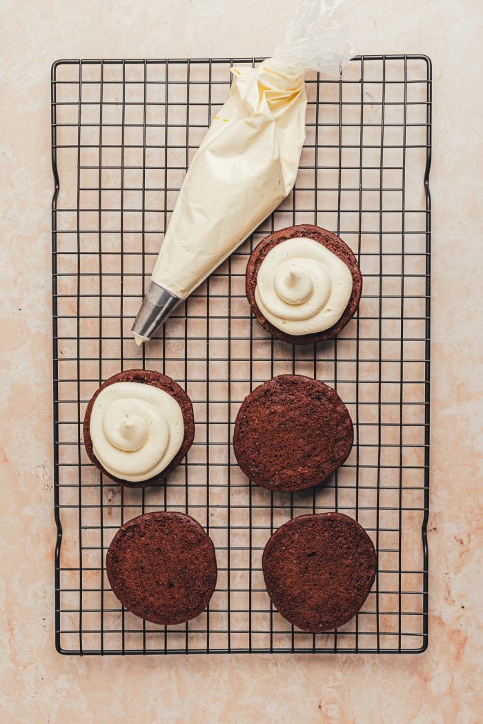 Whoopie pies on a cooling rack and frosting being applied to two Whoopie pie tops.